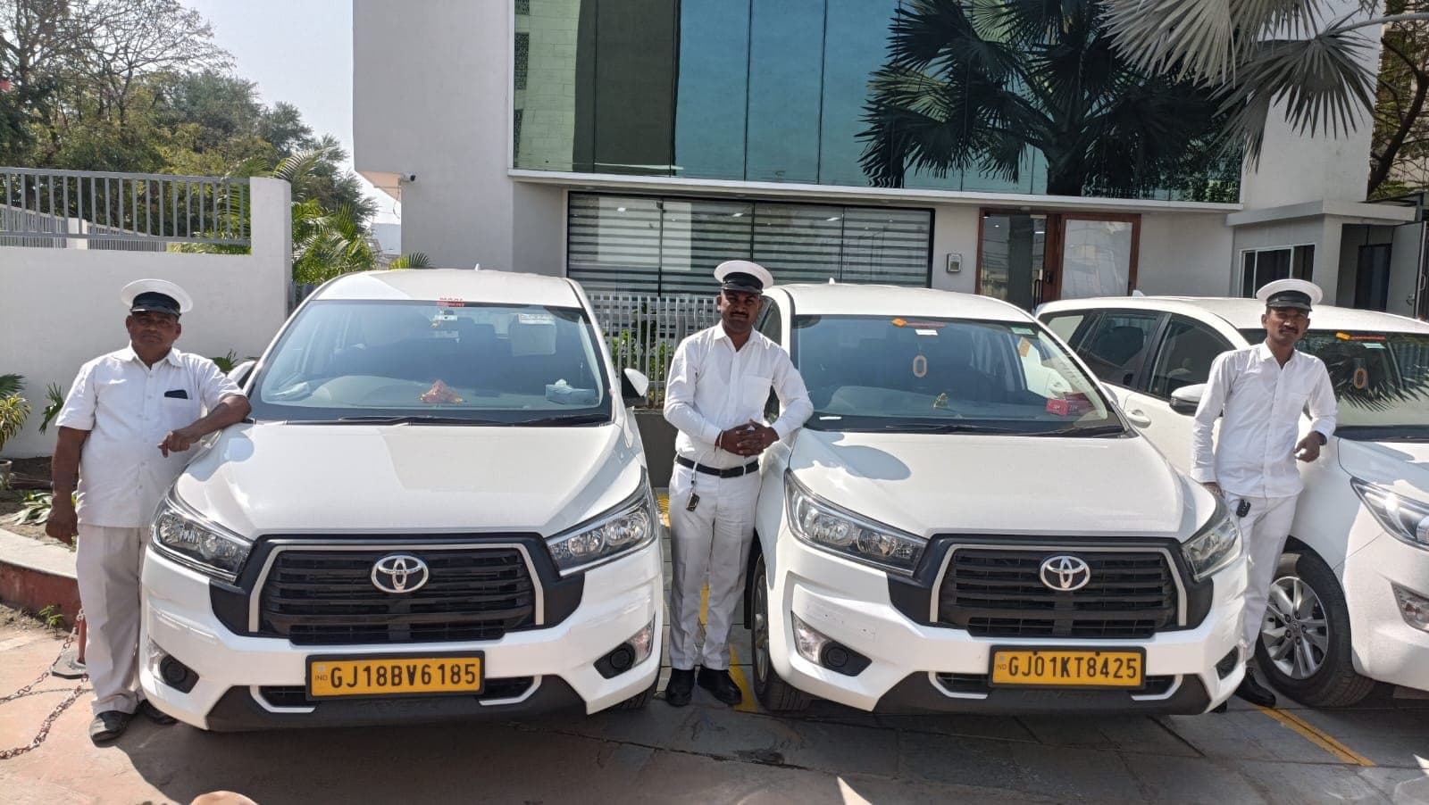 Vibrantcar chauffeurs in white uniforms and caps standing beside Toyota Innova Crysta cars